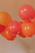 A cluster of red and orange balloons tied together and floating against a beige background.
