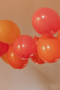A cluster of red and orange balloons tied together and floating against a beige background.