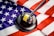 A wooden gavel with a brass band rests on a dark sound block, set against the backdrop of a United States flag. The flag features the familiar red and white stripes and white stars on a blue field, creating a strong visual association with American concepts of law and justice.