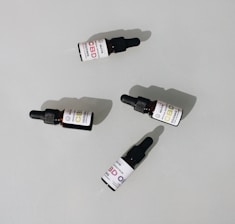 Several small dark bottles with dropper tops, labeled as CBD oil, are placed on a plain surface. The labels display different dosages and have a clean, minimalist design.