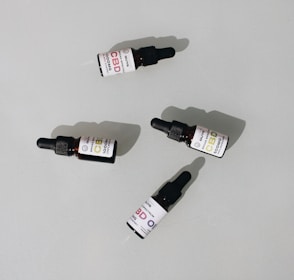 Several small dark bottles with dropper tops, labeled as CBD oil, are placed on a plain surface. The labels display different dosages and have a clean, minimalist design.