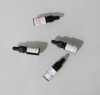 Several small dark bottles with dropper tops, labeled as CBD oil, are placed on a plain surface. The labels display different dosages and have a clean, minimalist design.