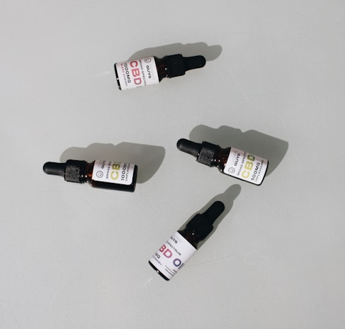 Several small dark bottles with dropper tops, labeled as CBD oil, are placed on a plain surface. The labels display different dosages and have a clean, minimalist design.