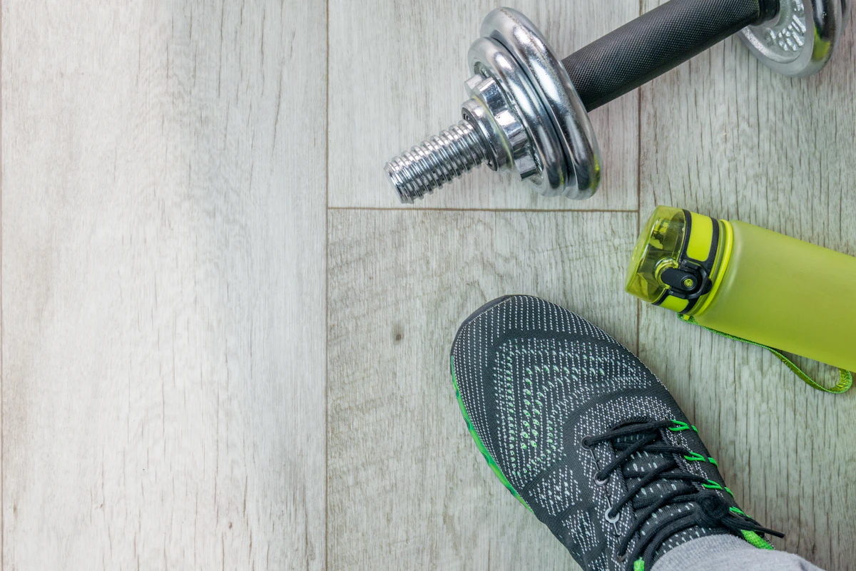 Buty sportowe, hantle i butelka wody na drewnianej podłodze