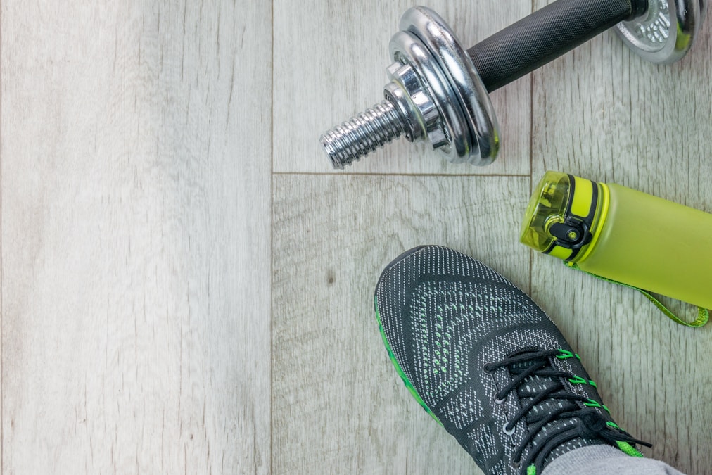 Training shoes, a dumbbell and a water bottle on a wooden floor