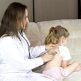 a woman in a white lab coat sitting on a couch with a little girl