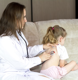 a woman in a white lab coat sitting on a couch with a little girl