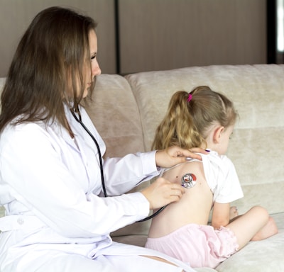 a woman in a white lab coat sitting on a couch with a little girl