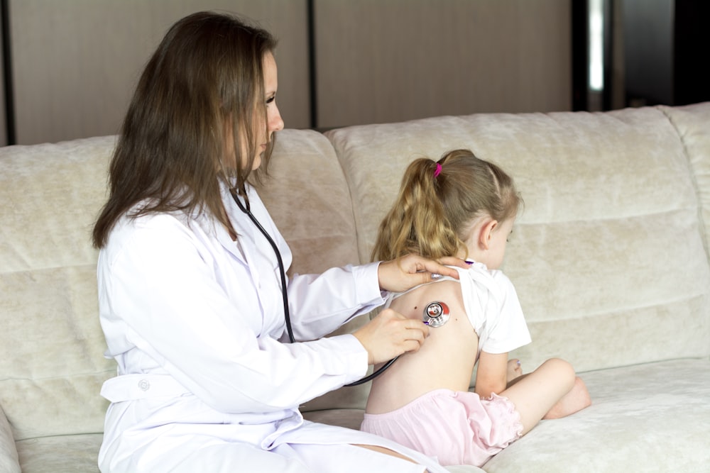 Eine Frau im weißen Laborkittel sitzt mit einem kleinen Mädchen auf einer Couch