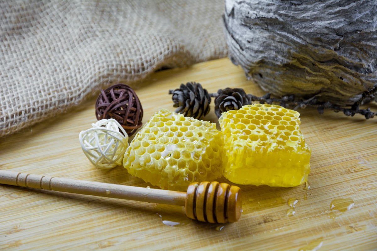 Cut honeycomb and a wooden honey dipper on a board beside hessian