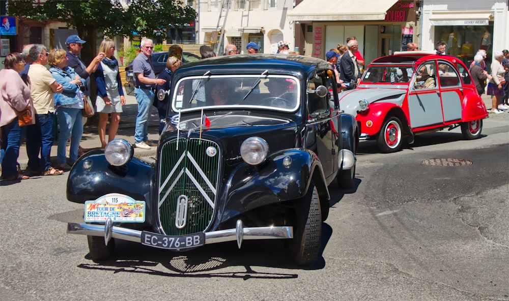 a vintage car driving down a street next to a crowd of people