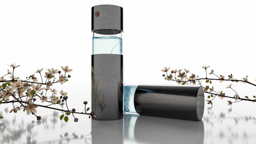 A sleek, modern perfume bottle with a transparent section showing light blue liquid, surrounded by delicate flowering branches. The design is minimalistic and elegant, suggesting luxury and sophistication.