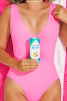 A person in a pink swimsuit is holding a can of Positive Energy drink labeled 'Tropical Bliss,' with a background featuring a pink towel. The person is wearing a pearl necklace and silver bracelets, and has a light tan complexion.