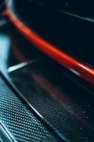 A close-up view featuring a glossy, textured carbon fiber material, highlighted by a striking red stripe. The image captures the sleek and modern design elements.
