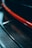 A close-up view featuring a glossy, textured carbon fiber material, highlighted by a striking red stripe. The image captures the sleek and modern design elements.