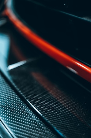 A close-up view featuring a glossy, textured carbon fiber material, highlighted by a striking red stripe. The image captures the sleek and modern design elements.