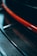 A close-up view featuring a glossy, textured carbon fiber material, highlighted by a striking red stripe. The image captures the sleek and modern design elements.