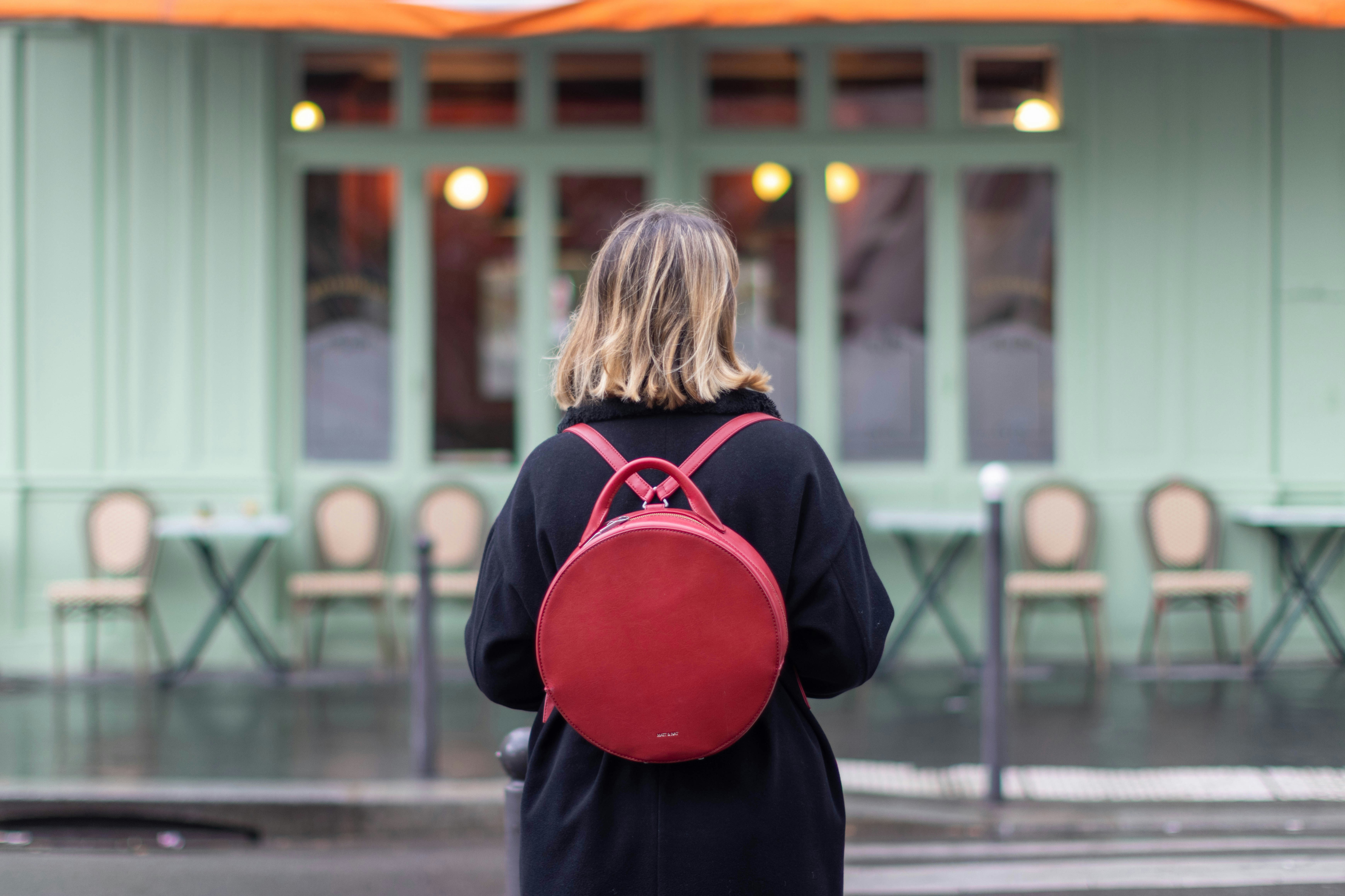 a woman with a red backpack walking down the street, Parisian girl in front of a green facade with a red backpack