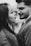 A couple facing each other closely, suggesting intimacy and affection. The woman has long hair and is wearing a textured garment, while the man has a neatly trimmed beard and is dressed in a suit. The image is in black and white, emphasizing contrast and depth.
