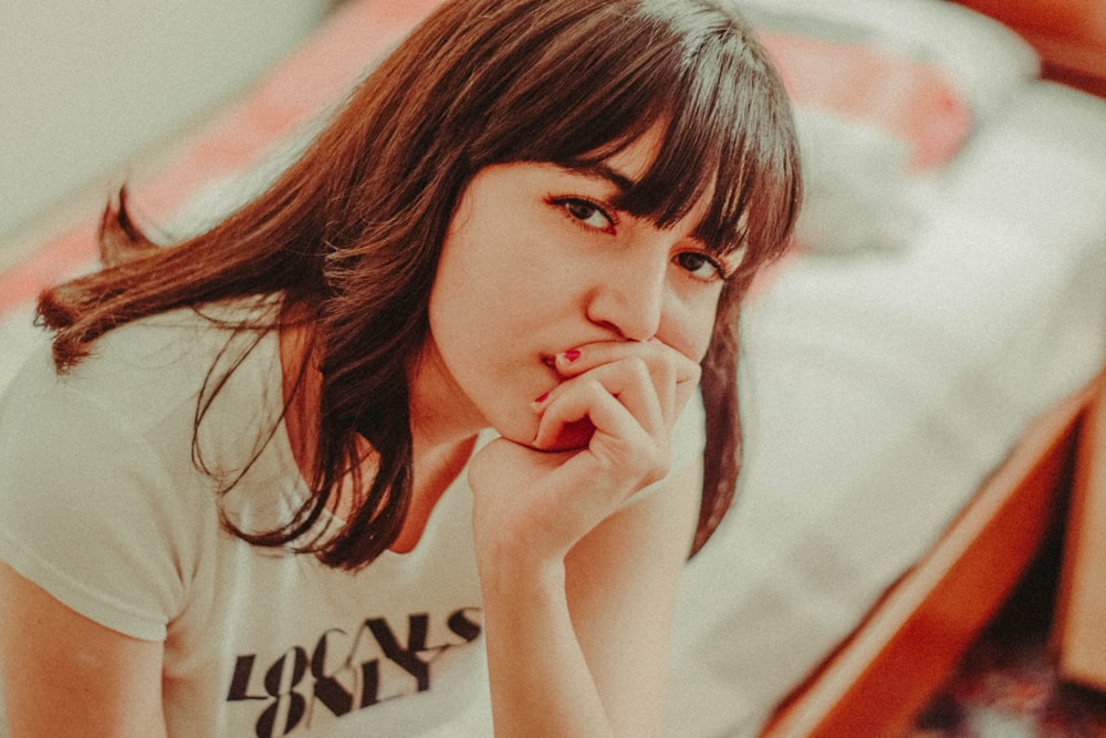 a woman sitting on a bed with her hand on her mouth