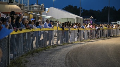 A lively crowd gathering around the race track with faint gold and purple decorations.
