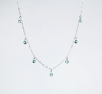 a silver necklace with green beads on a white background