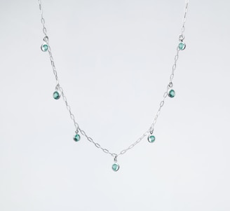 a silver necklace with green beads on a white background