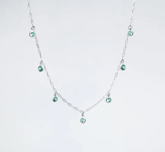 a silver necklace with green beads on a white background