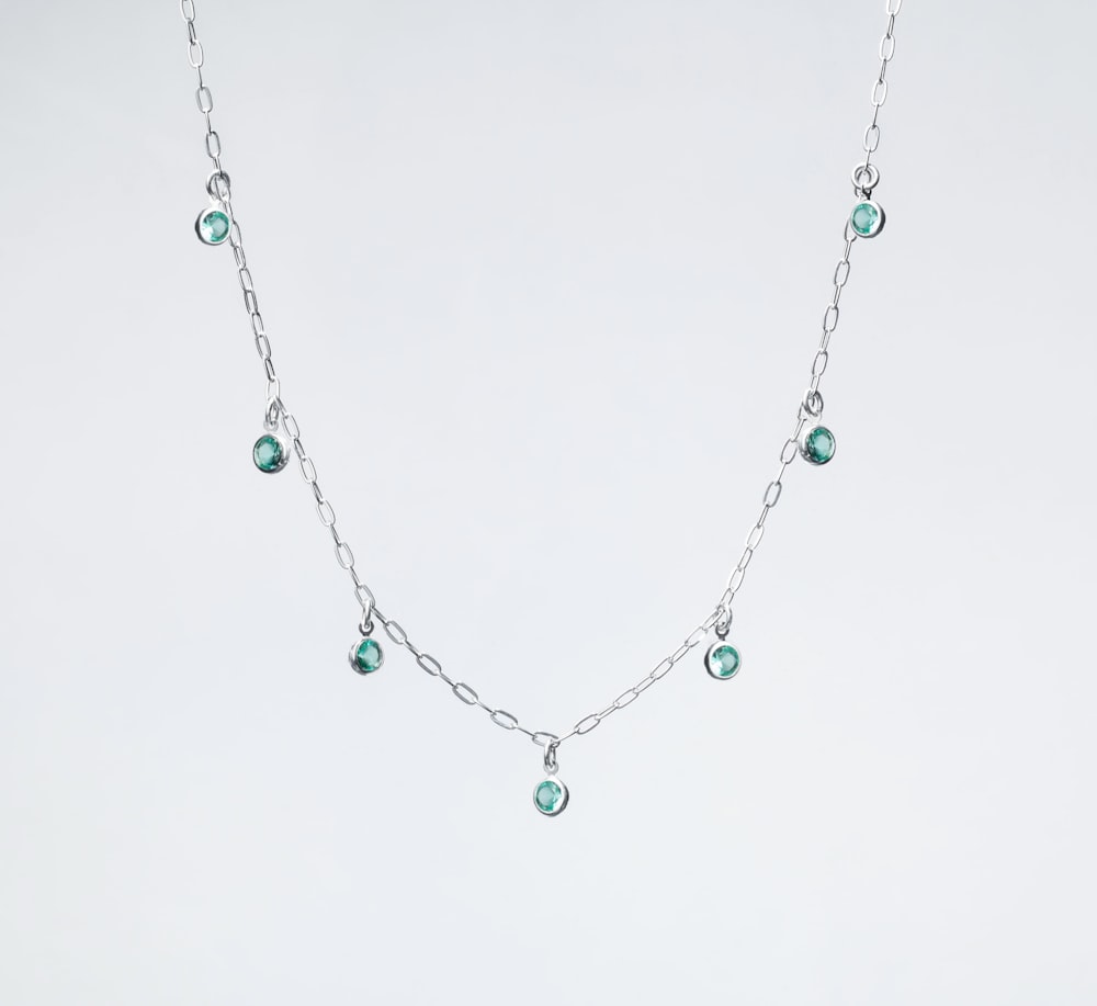 a silver necklace with green beads on a white background