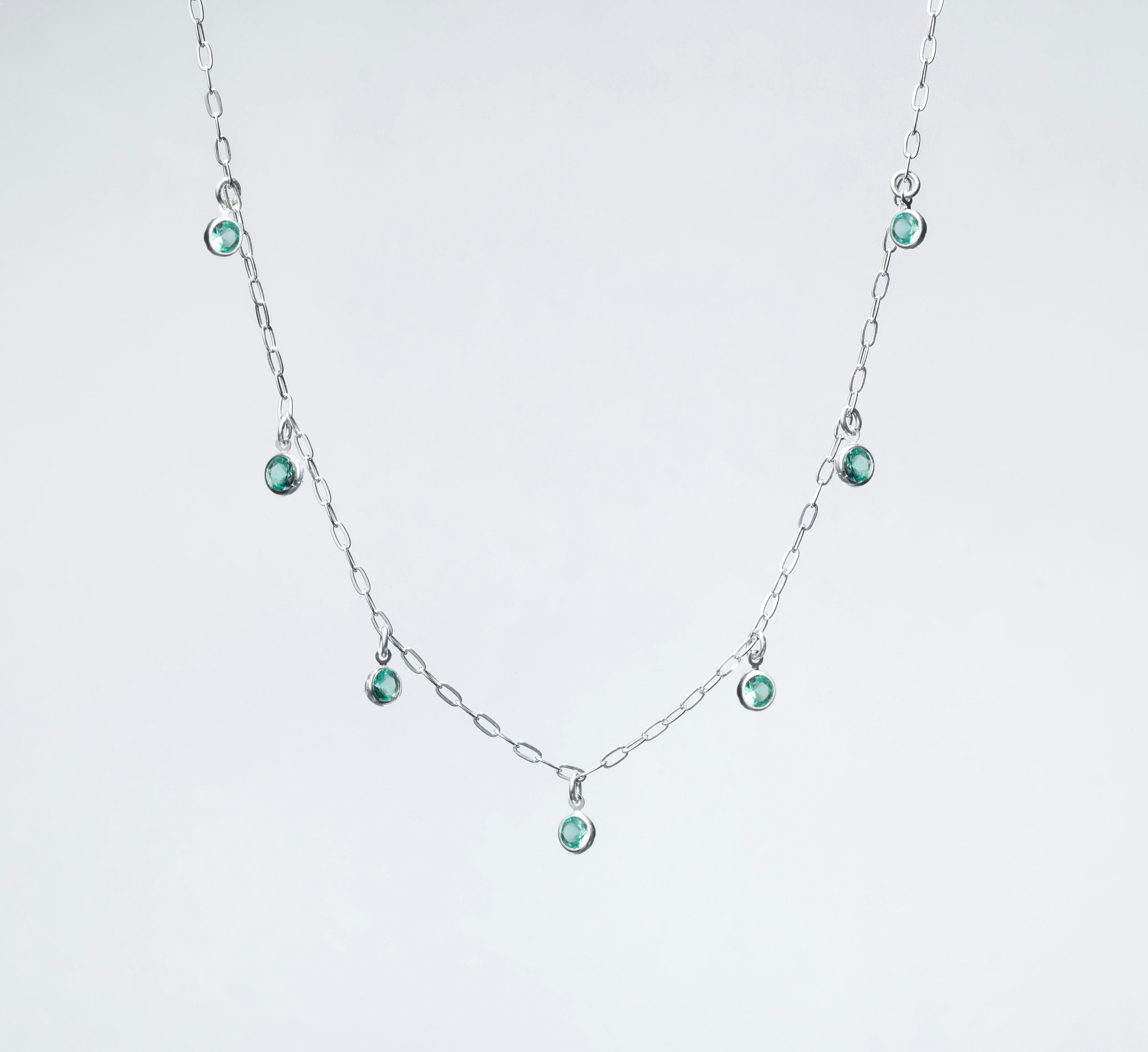 A silver necklace in bright plain background with small green gems