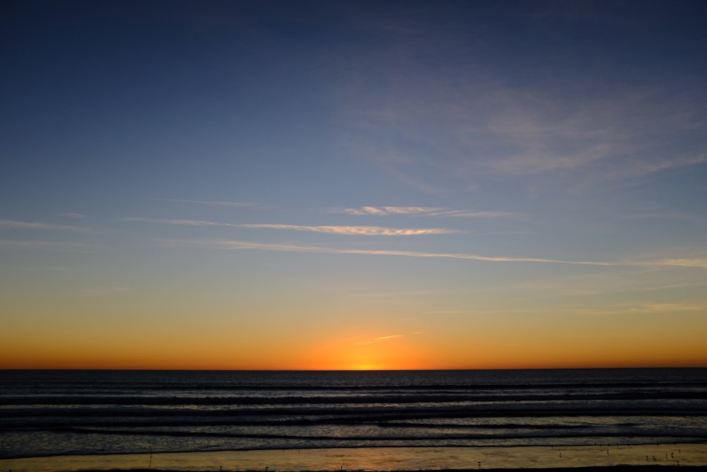 the sun is setting over the ocean on the beach