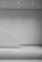 A minimalist, monochromatic interior space featuring a clean, angular design with a diagonal wall or partition. The scene is well-lit by ceiling spotlights, and the floor is covered with a textured surface.