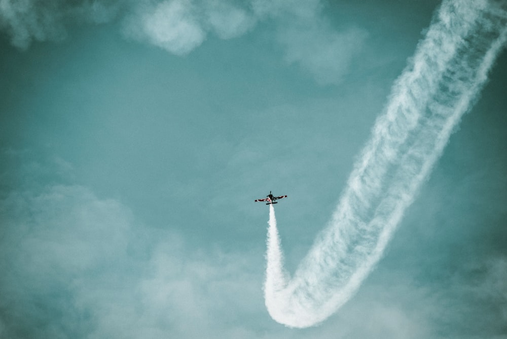 a plane flying in the sky leaving a trail of smoke behind it