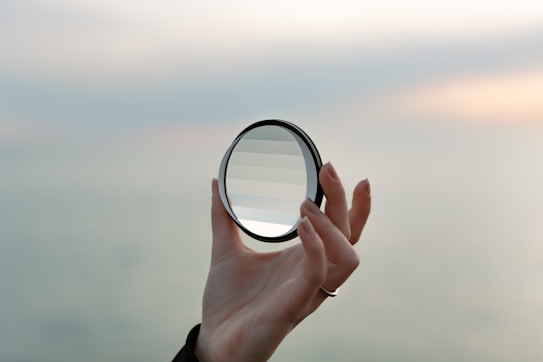 a hand holding a magnifying glass over a body of water