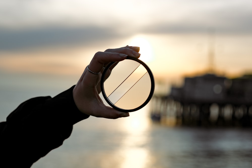 a person holding a circular object in front of a body of water