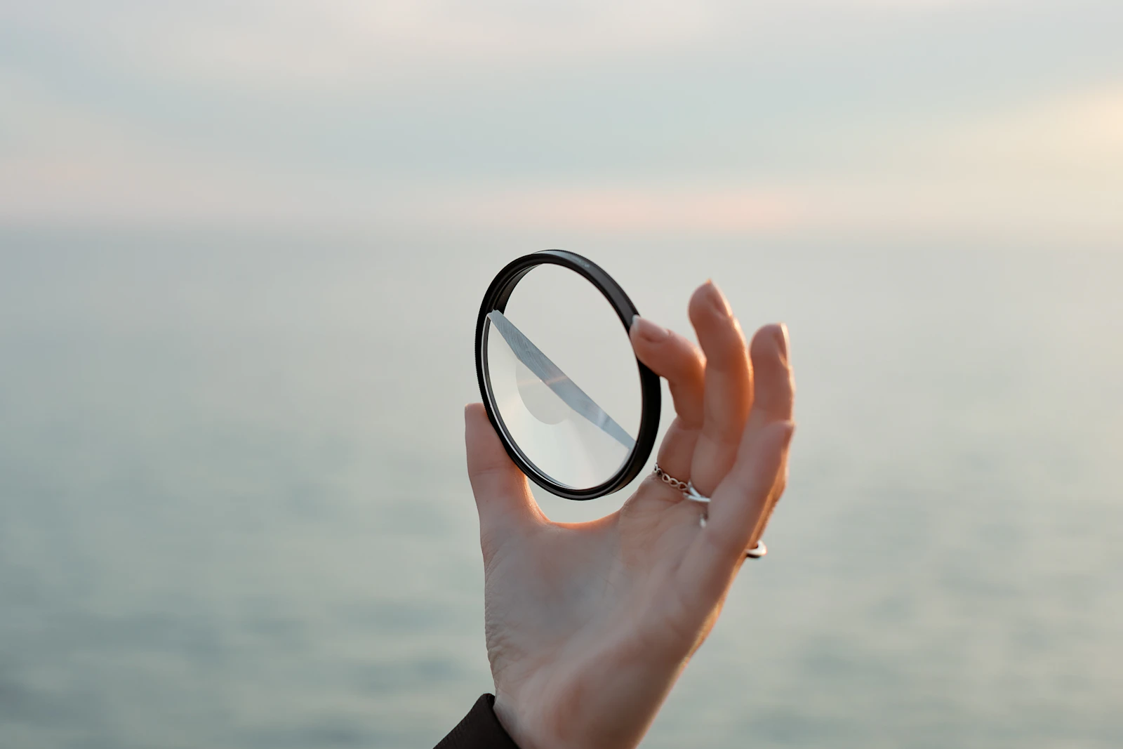 A hand holding a small round mirror up against a bright sky