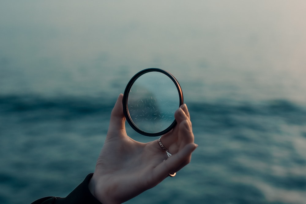 a hand holding a magnifying glass over a body of water