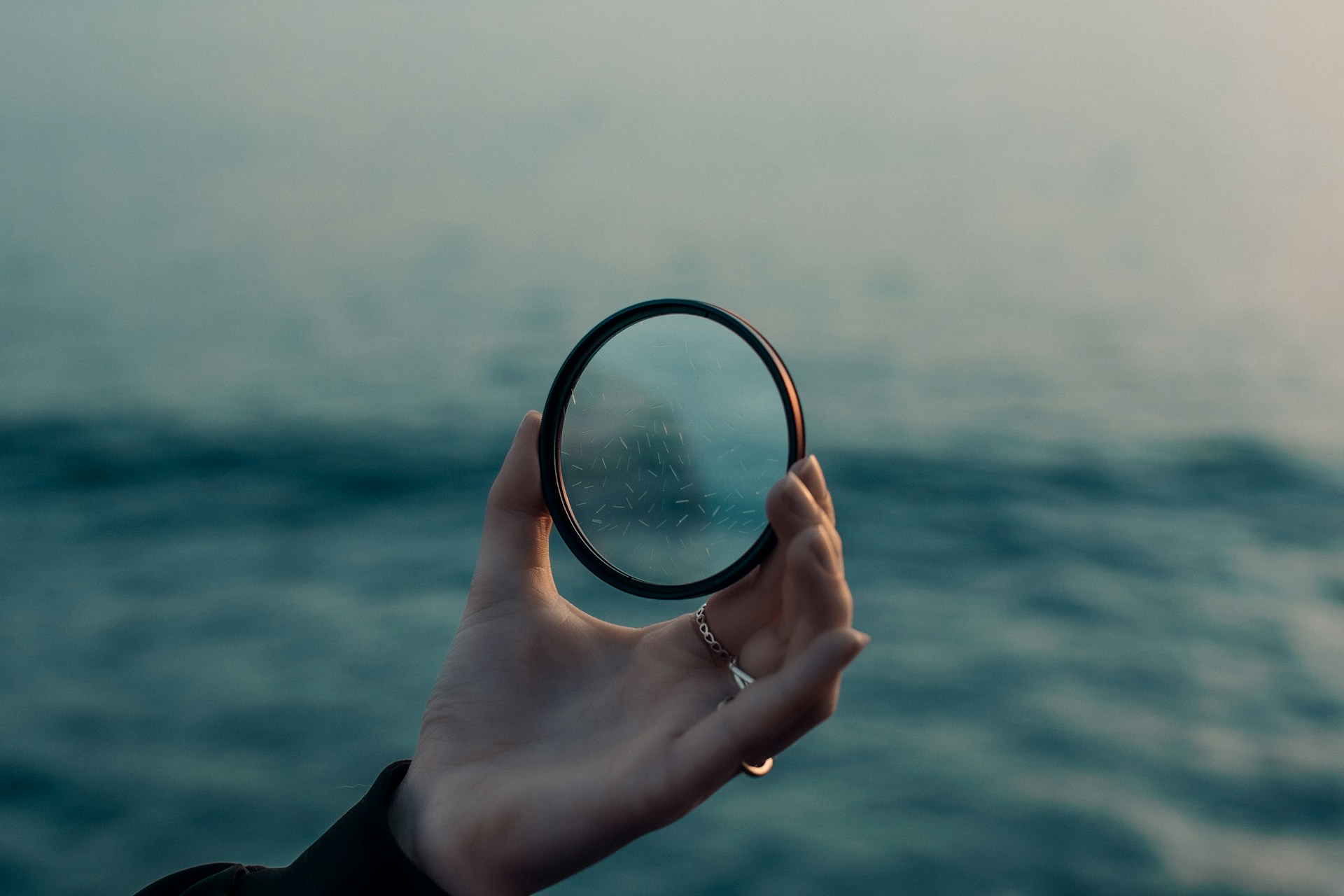 a hand holding a magnifying glass over a body of water