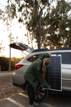Technician installing an electric vehicle charger with solar panels visible on the roof in the background.