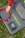 A hand in a red sleeve is arranging red electrical cable on a grey fabric mat. The mat features the branding 'Newpowa' in bright green text. A small electronic device, possibly a solar charge controller, is placed on the mat next to the cable. The scene is set outdoors, as indicated by the grass surrounding the mat.