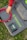 A hand in a red sleeve is arranging red electrical cable on a grey fabric mat. The mat features the branding 'Newpowa' in bright green text. A small electronic device, possibly a solar charge controller, is placed on the mat next to the cable. The scene is set outdoors, as indicated by the grass surrounding the mat.