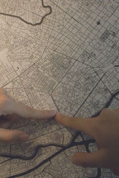 Two hands are pointing on a detailed map, with visible roads and geographical features. The map has a grid-like appearance and includes various city streets and landmarks.