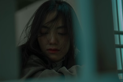 A contemplative woman with long dark hair sits with her eyes closed. The image has a muted color palette with a soft focus, suggesting introspection or peace.