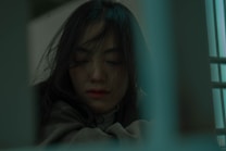 A contemplative woman with long dark hair sits with her eyes closed. The image has a muted color palette with a soft focus, suggesting introspection or peace.
