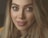 A close-up portrait of a woman with long hair and well-defined facial features. Her eyes are large and expressive, accompanied by full lips and neatly arched eyebrows. The lighting is soft, highlighting her smooth skin and creating a warm atmosphere.