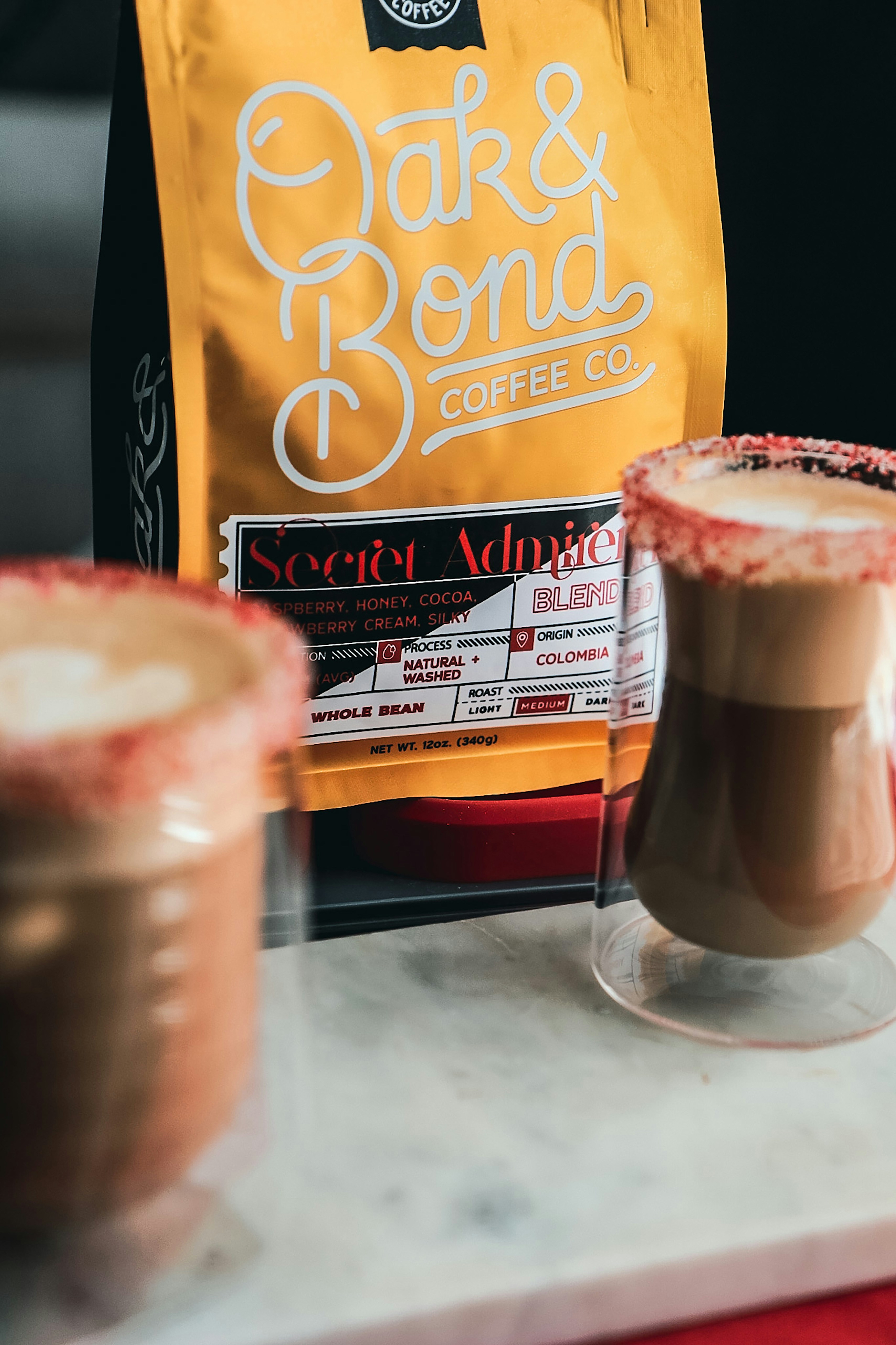 two cups of coffee sit on a counter next to a bag of coffee