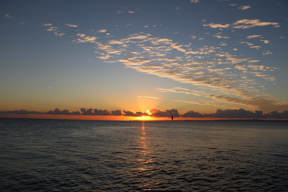 the sun is setting over the ocean with clouds in the sky