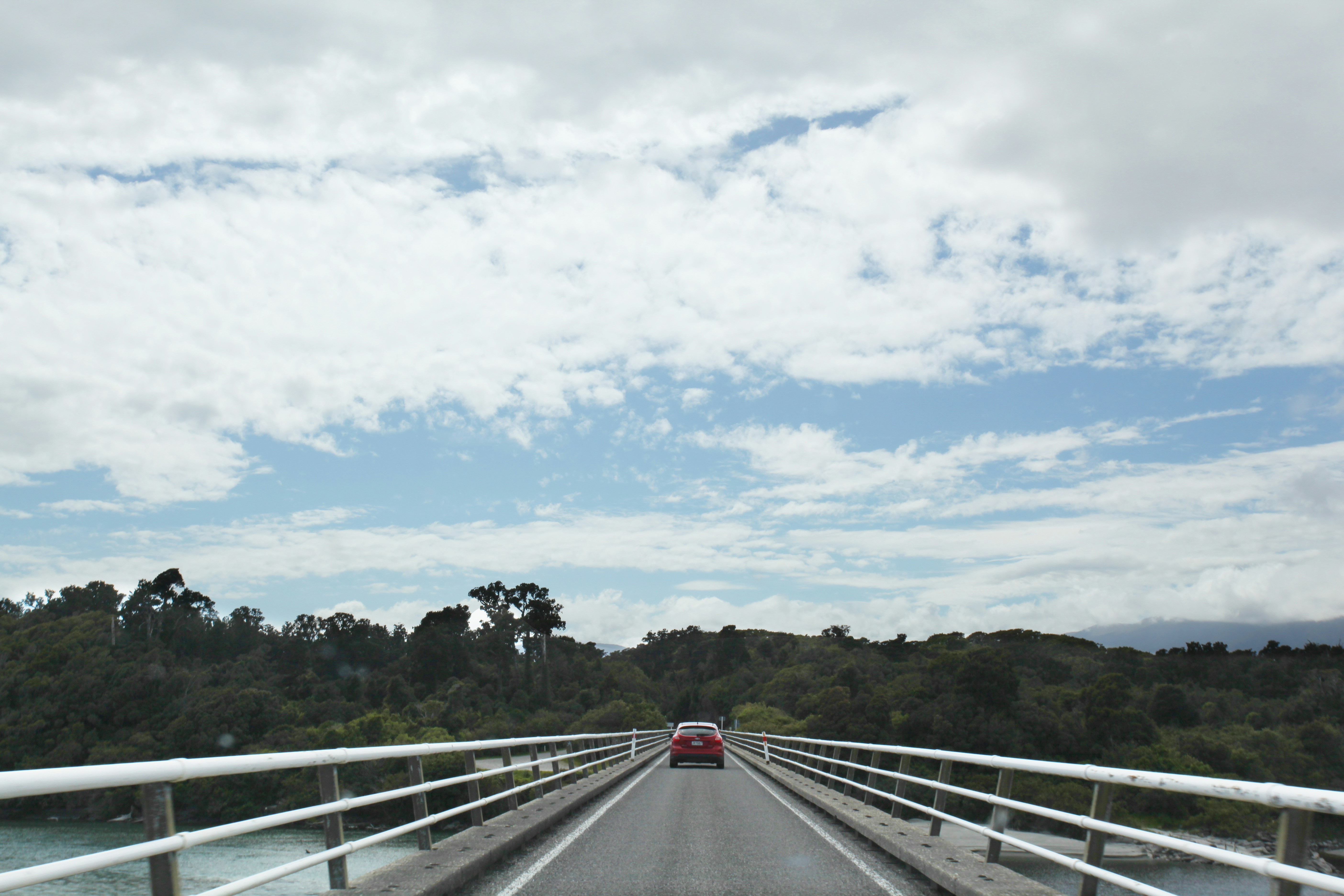 a red car driving across a bridge over a river, 