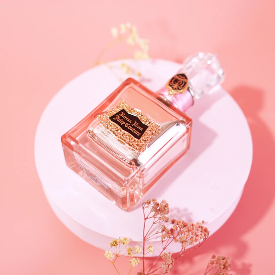 A delicate glass bottle of floral perfume with soft pink hues resting on a vintage wooden table.