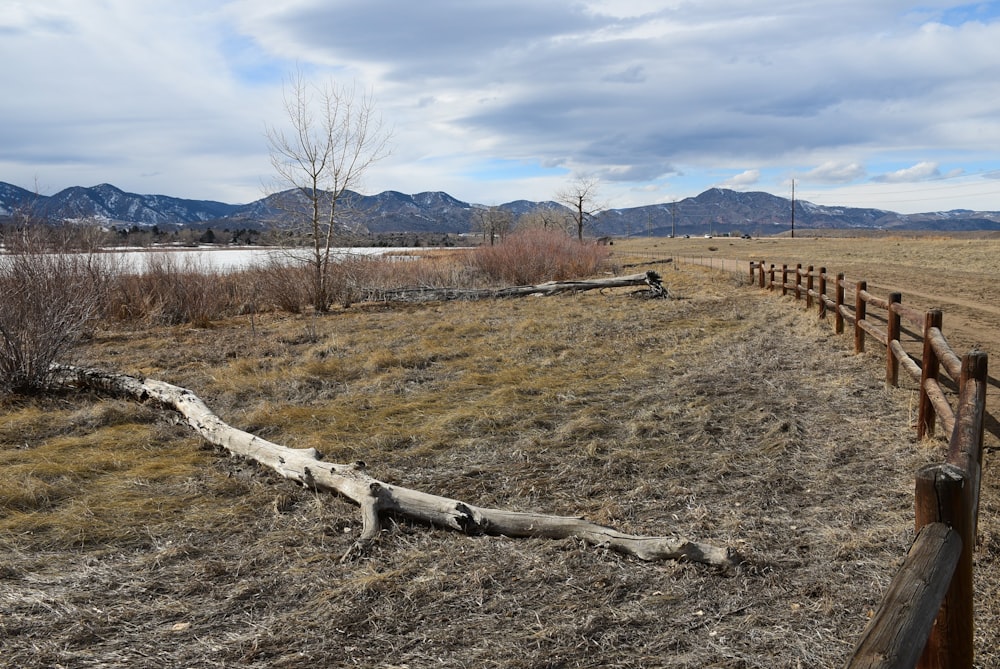 a wooden fence in a field with mountains in the background